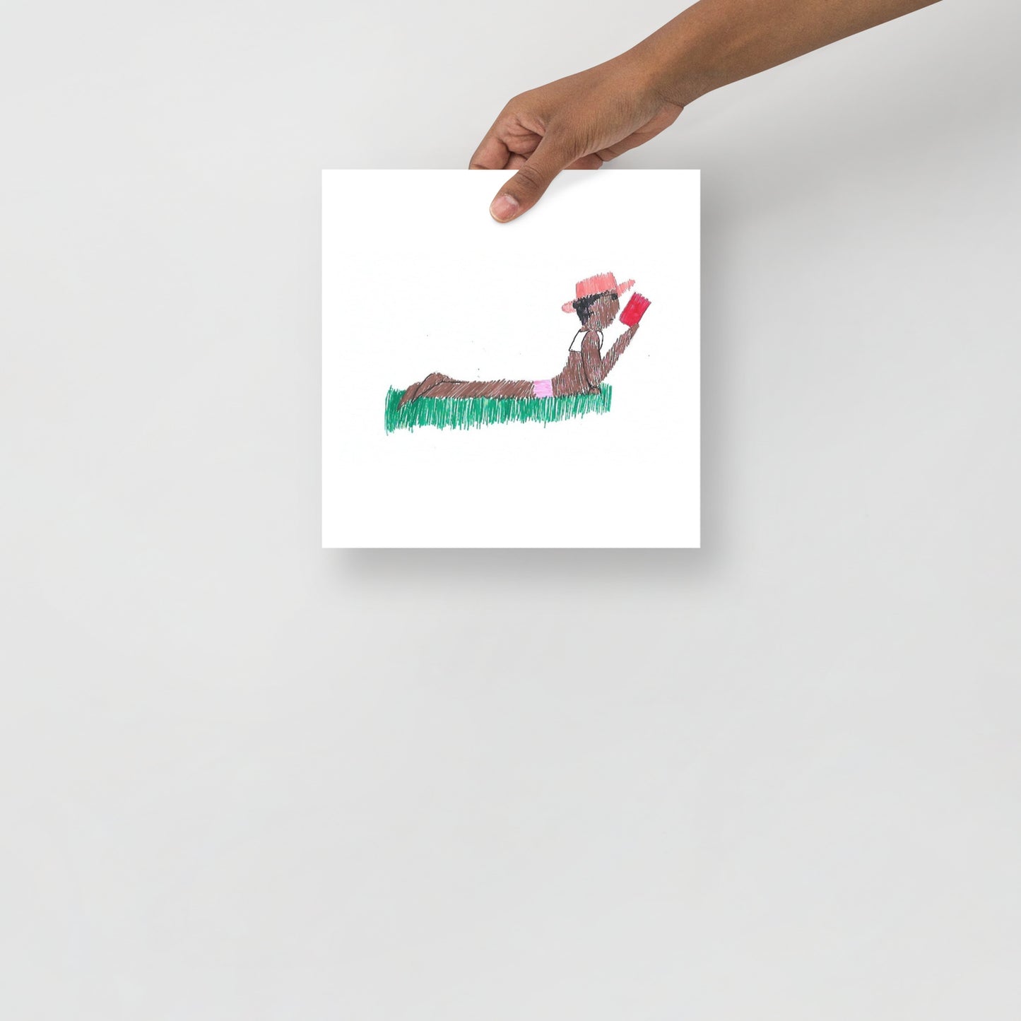 This image shows an art print of a square artwork featuring a person lying in grass, wearing a hat and reading a book, against a plain white background. The scene feels peaceful and relaxed.