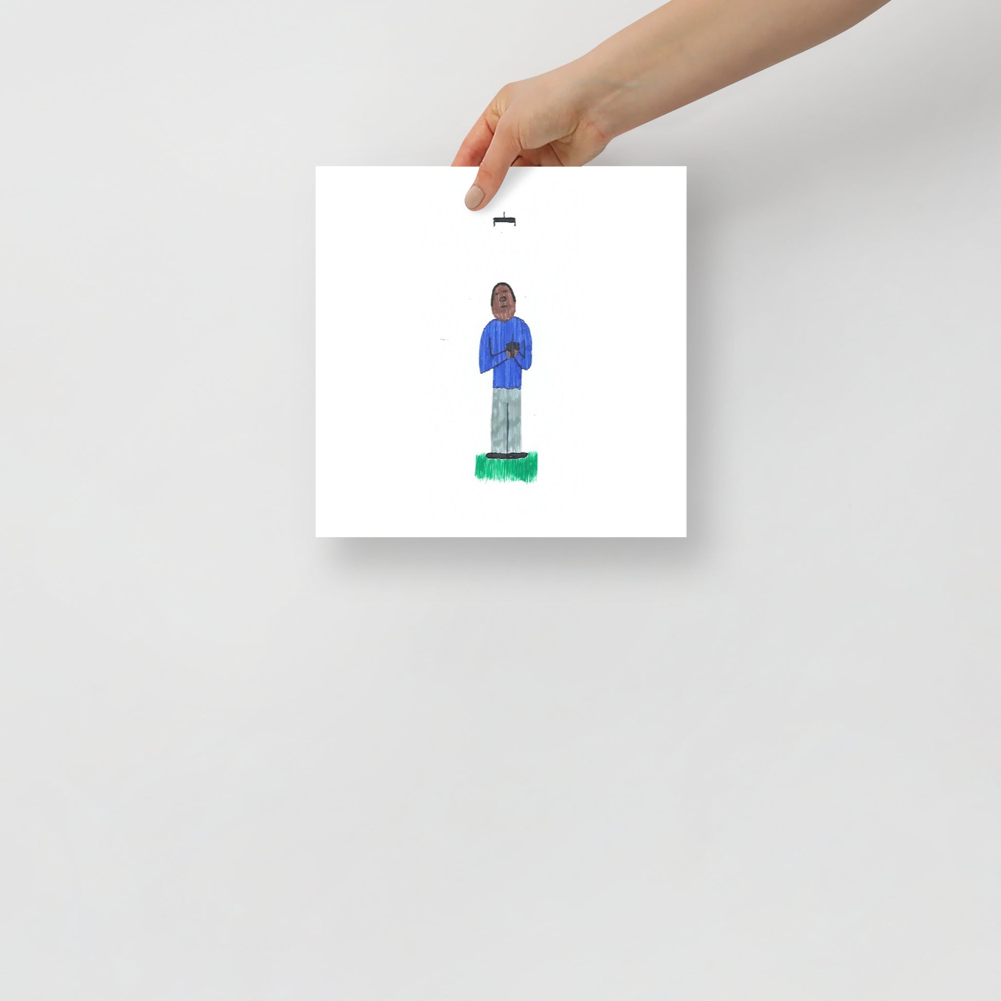 This image shows an art print of a square illustration featuring a figure in a blue outfit standing on green ground flying a drone against a white background. Minimalist and simple design.