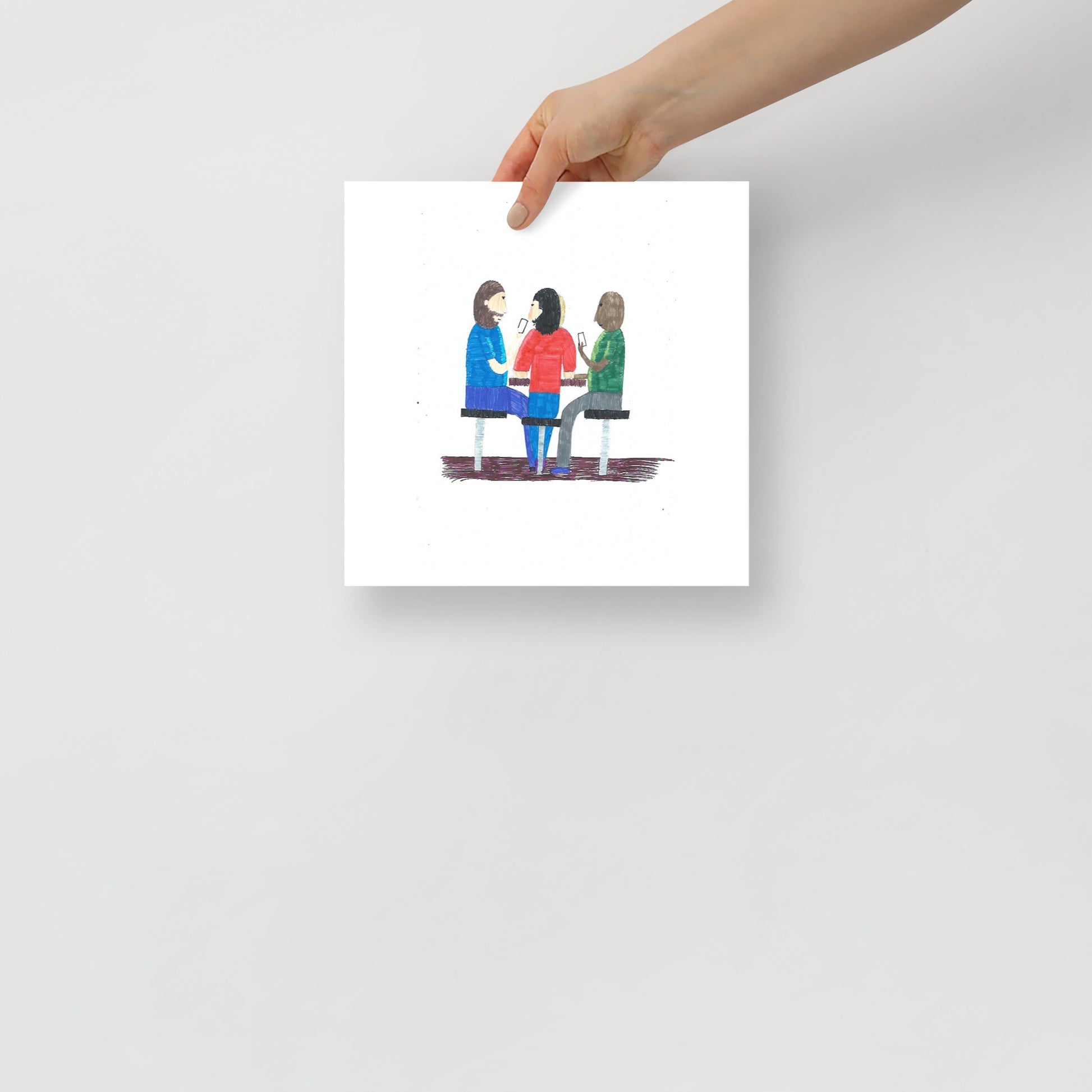 This image shows a square art print of three people seated at a table, engaging in a card game and conversation. The image conveys a sense of collaboration and connection.