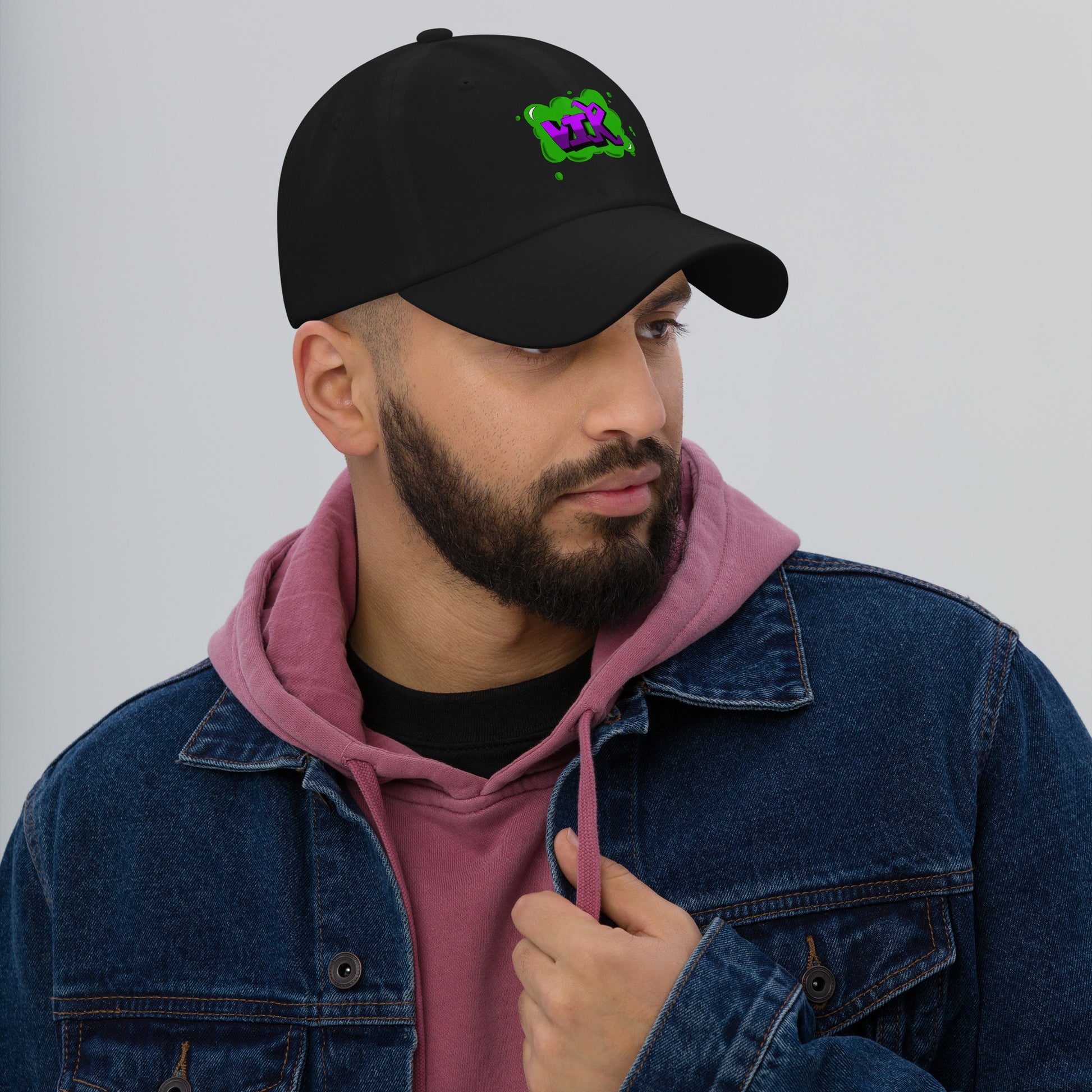 This image displays a man wearing a black baseball cap with a green and purple graffiti style design saying VIK embroidered on it